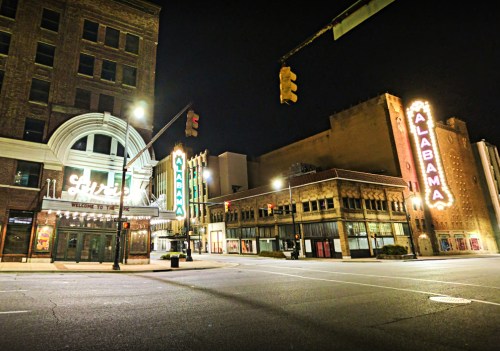 Historic theaters lit up at night, showcasing vibrant neon signs in a quiet urban street.