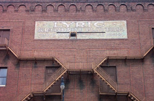 Faded mural on a brick building featuring the word "LYRIC" and fire escape stairs.