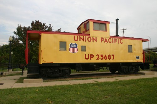 A yellow Union Pacific caboose, labeled UP 25687, displayed on a grassy area with trees in the background.