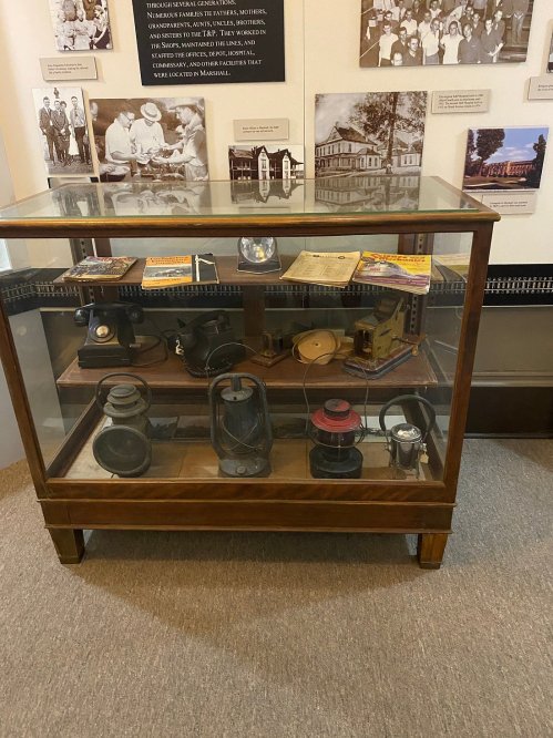 Display case featuring vintage communication devices and historical documents, with photos in the background.