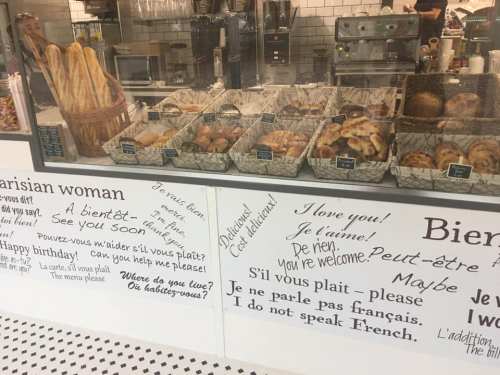 A bakery display with various pastries and bread, featuring handwritten signs in French and English welcoming customers.