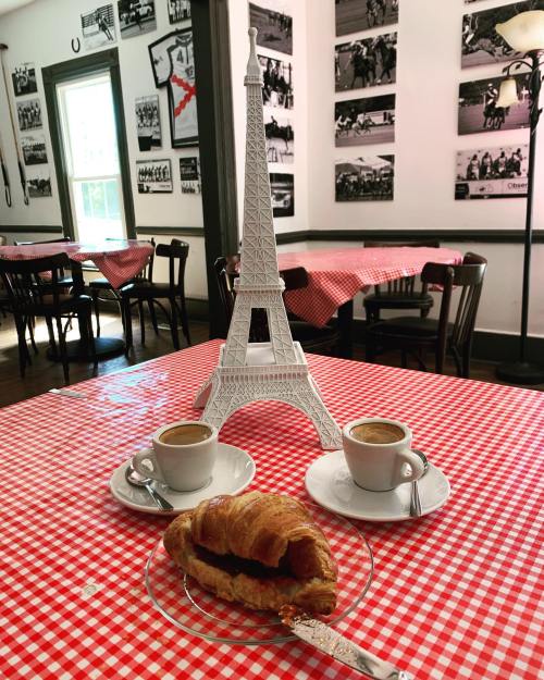 A table set with two espresso cups, a croissant, and a miniature Eiffel Tower, all on a red checkered tablecloth.
