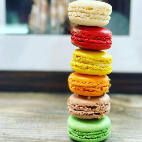 A colorful stack of six macarons in various flavors, arranged vertically on a wooden surface.