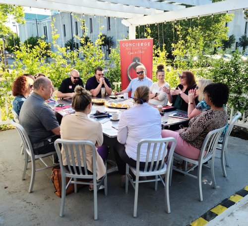 A group of people seated around a table outdoors, engaged in conversation with food and drinks.