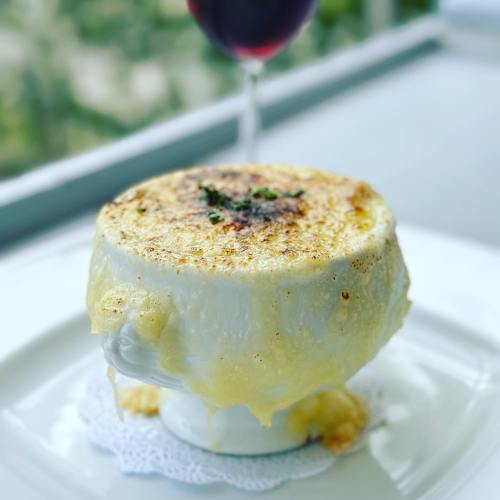 A creamy, cheesy dish in a decorative bowl, with melted cheese bubbling and dripping over the sides, served with a glass of wine.