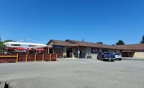 A building with a patio area, red umbrellas, and a parking lot under a clear blue sky.