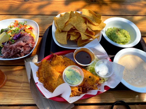 A vibrant meal featuring tacos, guacamole, chips, salsa, and a side of meat on a wooden table.