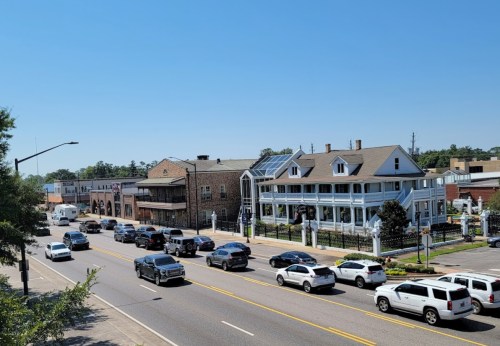 A busy street scene featuring cars, a historic building, and clear blue skies.