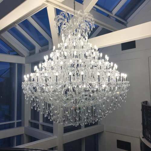 A large, elegant crystal chandelier with multiple lights hangs from a ceiling in a bright, modern space.