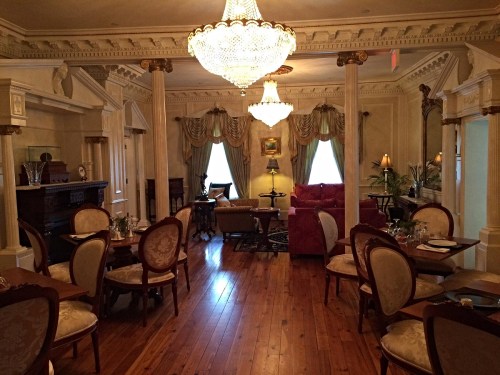 Elegant dining room with chandeliers, wooden floors, and plush seating, featuring ornate decor and soft lighting.