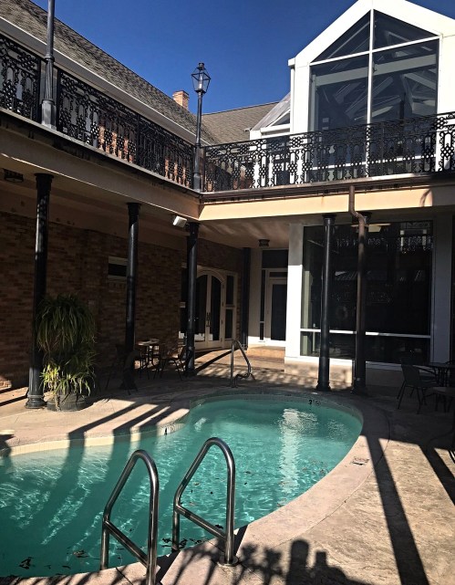 A serene courtyard with a small pool, surrounded by elegant architecture and shaded by tall columns.