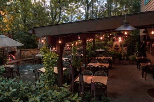 Cozy outdoor restaurant patio with string lights, tables, and lush greenery, creating a warm, inviting atmosphere.