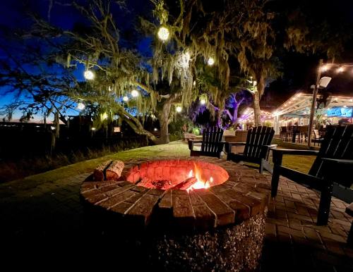 A cozy fire pit surrounded by chairs, with twinkling lights in trees and a serene evening sky in the background.
