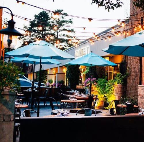 Outdoor dining area with teal umbrellas, string lights, and lush greenery, creating a cozy atmosphere.