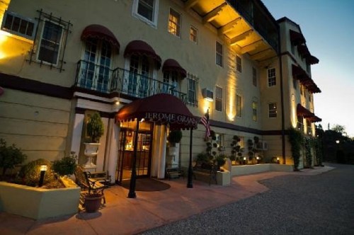 Historic hotel entrance with warm lighting, awnings, and potted plants, set against a twilight sky.