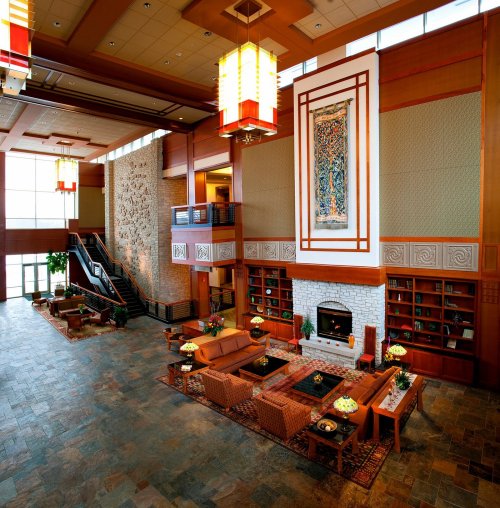A spacious hotel lobby with modern decor, comfortable seating, a fireplace, and large windows letting in natural light.