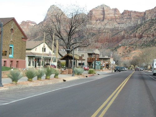 A scenic view of a small town street with shops, trees, and mountains in the background.