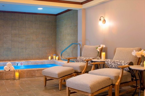 A serene spa area featuring two lounge chairs, a small pool, and soft lighting with candles and decorative flowers.