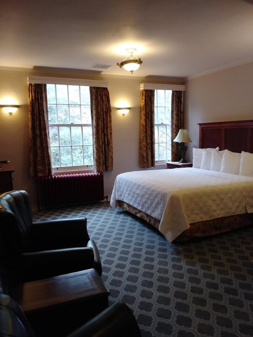 Cozy hotel room with a large bed, two armchairs, and large windows letting in natural light.