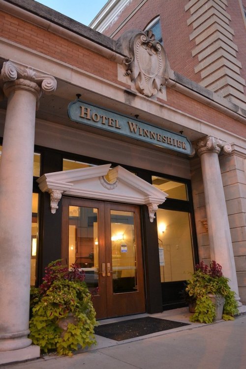 Entrance of Hotel Winneshiek featuring decorative columns and potted plants, with a vintage sign above the doors.