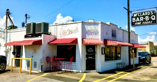 Exterior of McClard's Bar-B-Q, featuring a white building with red awnings and a sign, under a clear blue sky.