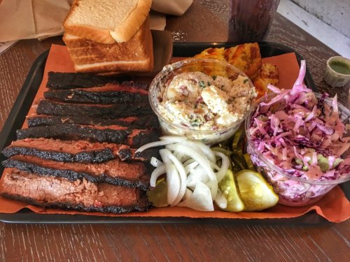 A platter of smoked brisket, pickles, onions, coleslaw, potato salad, and slices of toasted bread.