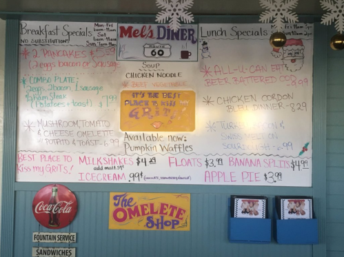 Menu board at Mel's Diner featuring breakfast and lunch specials, including pancakes, omelettes, and milkshakes.