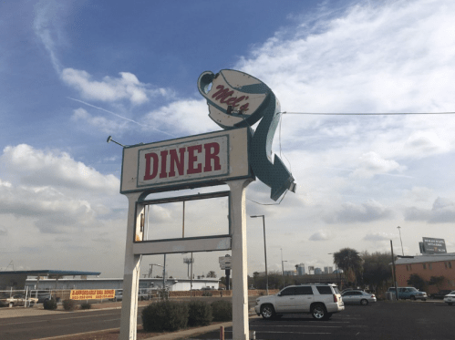 Sign for "Mike's Diner" with a fish design, set against a cloudy sky and parking lot.
