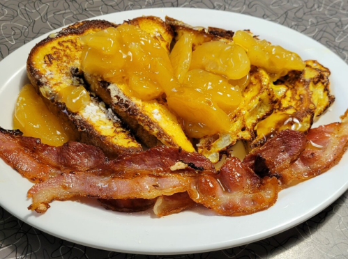A plate of French toast topped with orange slices and served with crispy bacon.