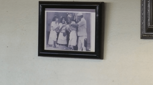 Black and white photo of four people in vintage clothing, smiling and interacting in a retro setting, framed on a wall.