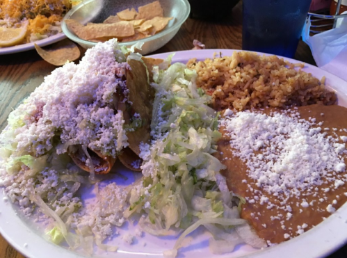A plate of tacos topped with lettuce and cheese, served with rice and refried beans on the side.