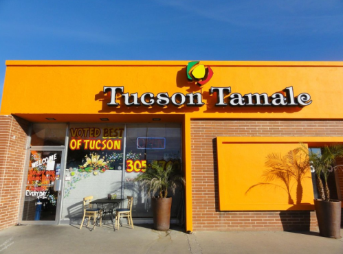 Bright orange storefront of Tucson Tamale, featuring a "Voted Best of Tucson" sign and outdoor seating.