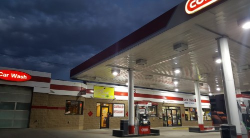 A gas station with a car wash, illuminated at dusk, featuring a convenience store and a restaurant sign.