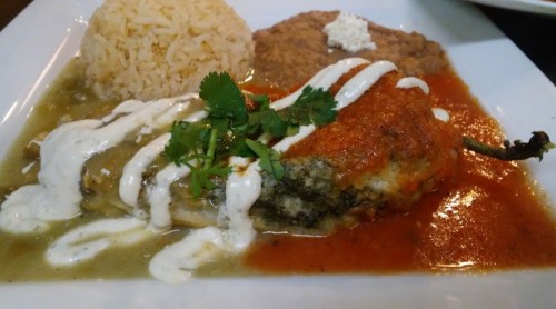 A plate featuring a stuffed chili pepper with sauces, rice, and refried beans, garnished with cilantro.