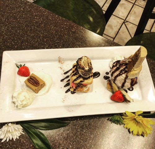 A dessert plate featuring two ice cream scoops, strawberries, chocolate drizzle, and a small piece of cake.
