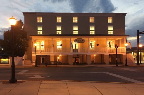 A historic building with illuminated windows, featuring a porch and a sign that reads "Museum," at dusk.