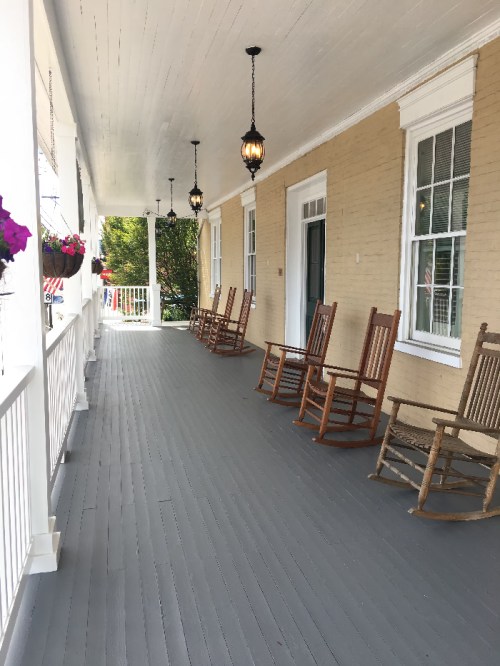A porch with rocking chairs and hanging lanterns, featuring potted flowers along the railing.