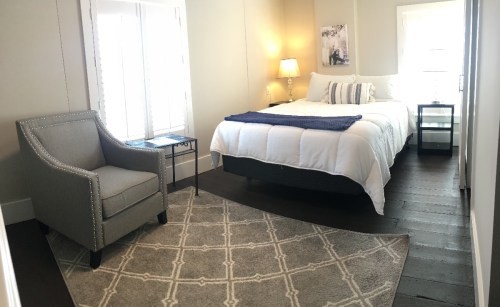 Cozy bedroom featuring a bed, armchair, nightstand, and large window with natural light.