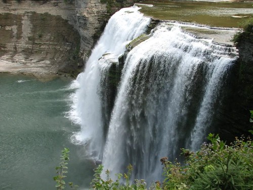 A majestic waterfall cascading over rocky cliffs into a serene green pool below, surrounded by lush vegetation.