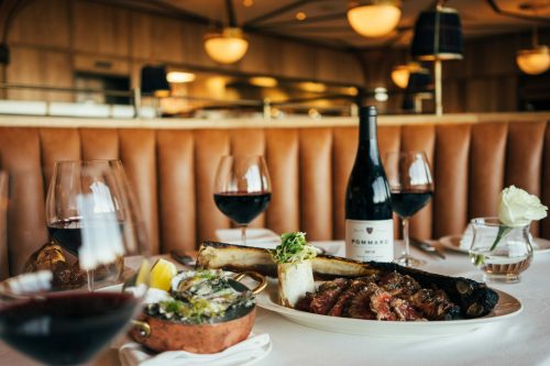 A table setting featuring a gourmet meal, red wine, and elegant decor in a restaurant.