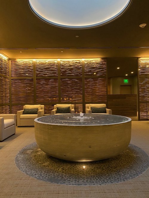 A serene spa interior featuring a round water feature, soft lighting, and comfortable seating.