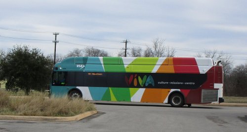 A colorful bus with "VIVA" branding parked on a road, surrounded by grass and trees under a cloudy sky.