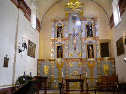 Interior of a church featuring a decorated altar with religious figures, gold accents, and soft lighting.