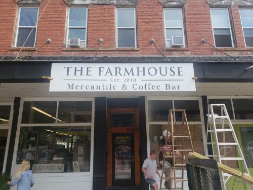 Sign for "The Farmhouse Mercantile & Coffee Bar" established in 2018, with people and ladders nearby.
