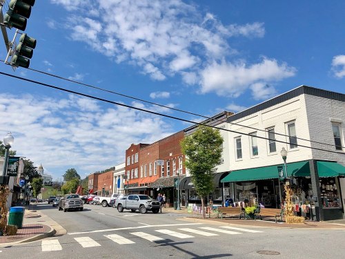 A quaint town street with shops, green awnings, and a blue sky dotted with clouds. Traffic lights and a crosswalk visible.