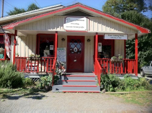 A charming wooden shop with red accents, featuring a welcoming entrance and flower pots on the porch.