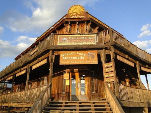 A rustic wooden building with multiple signs, featuring a mercantile and outdoor tour information on the Apache Trail.