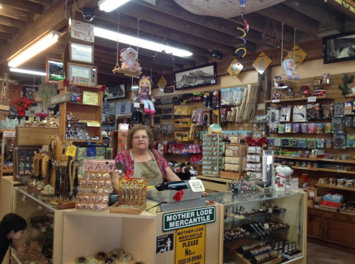 A woman stands behind a counter in a colorful gift shop filled with various souvenirs and decorations.