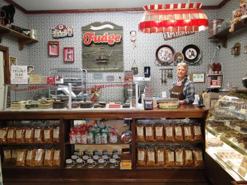 A cozy fudge shop with a smiling employee behind the counter, surrounded by jars of sweets and vintage decor.