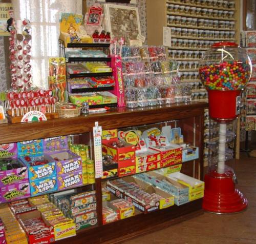 A vintage candy store display featuring colorful candies, a gumball machine, and various sweet treats in jars.